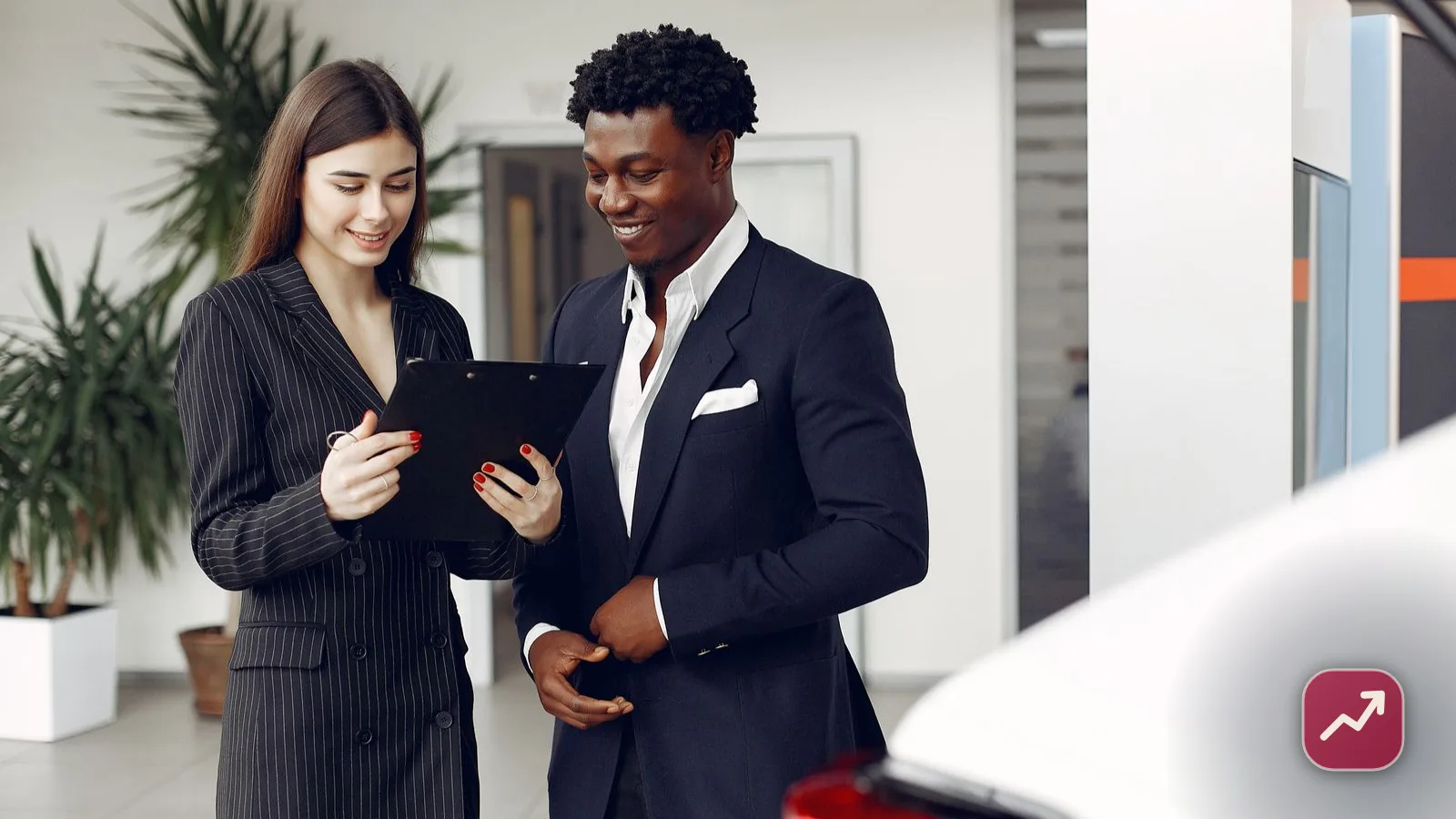 Une conseillère commerciale passe en revue le contrat d’une extension de garantie avec un client souriant dans un showroom.