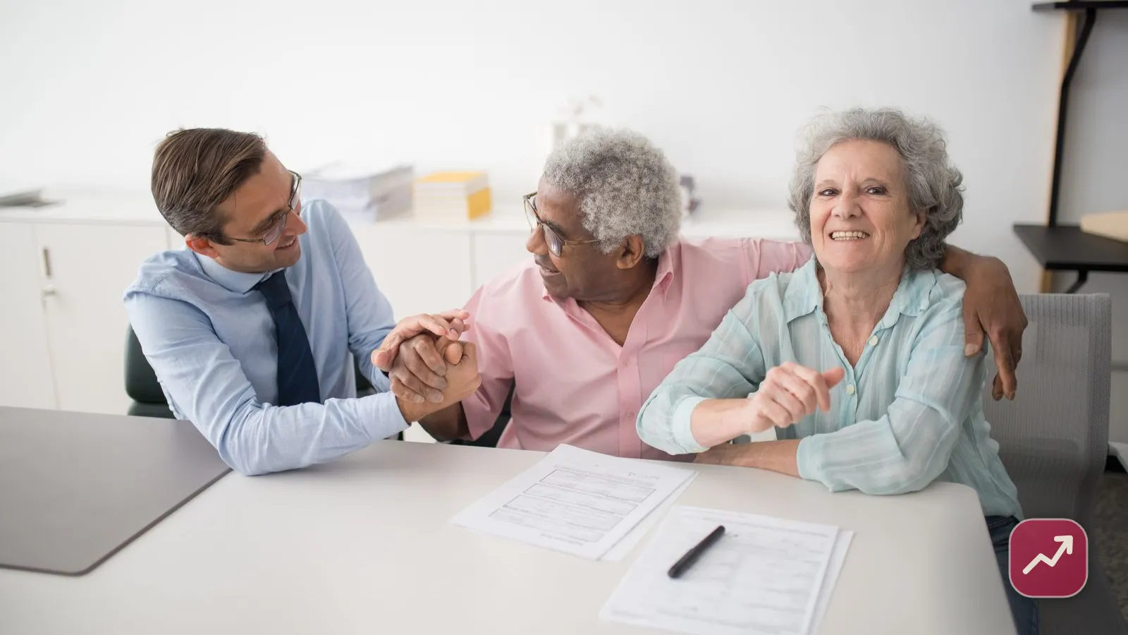 Un conseiller financier en rendez-vous avec un couple de seniors souriants devant des documents, illustrant comment décider si l’on a besoin d’un conseiller financier.