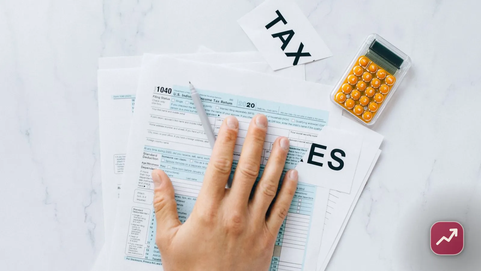 A hand filling out a tax return form next to a calculator and TAXES lettering, illustrating how to file your taxes.