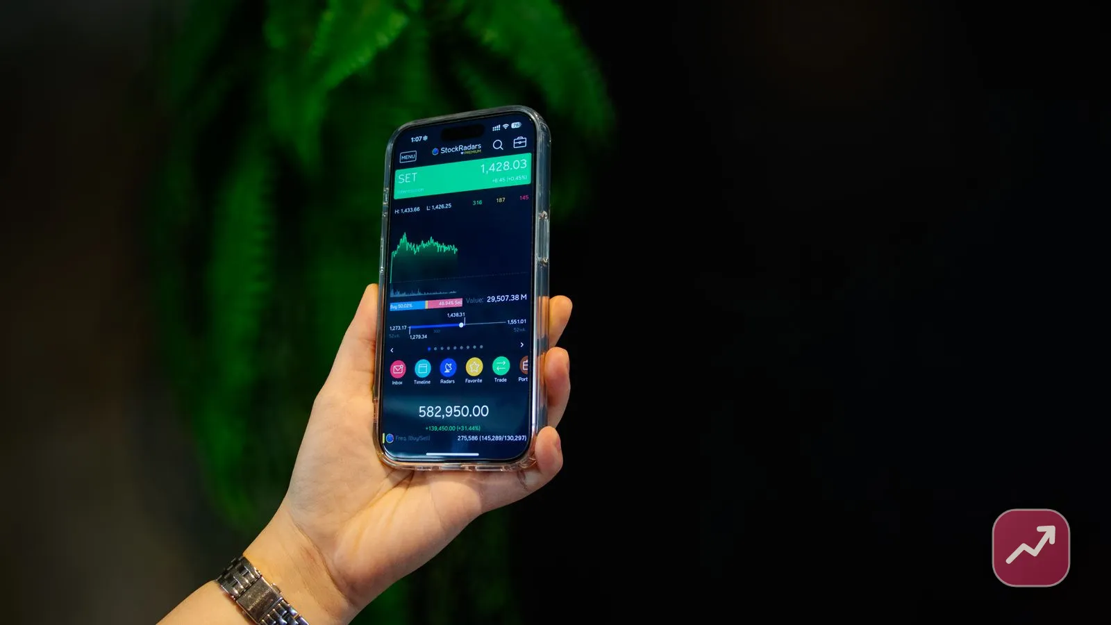 A hand holding a phone showing a rising stock market app, illustrating how to invest in stocks as a beginner.