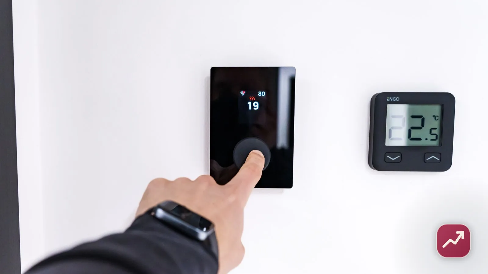 A hand setting a home thermostat to 19 degrees on a white wall, illustrating how to lower your electricity bill by controlling heating.