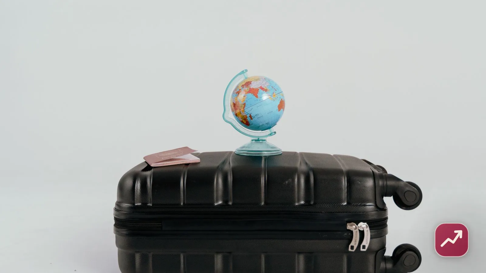 Un pasaporte y una tarjeta de embarque sobre una maleta con un pequeño globo terráqueo, que ilustran la preparación del viaje y por qué importa el seguro de viaje.