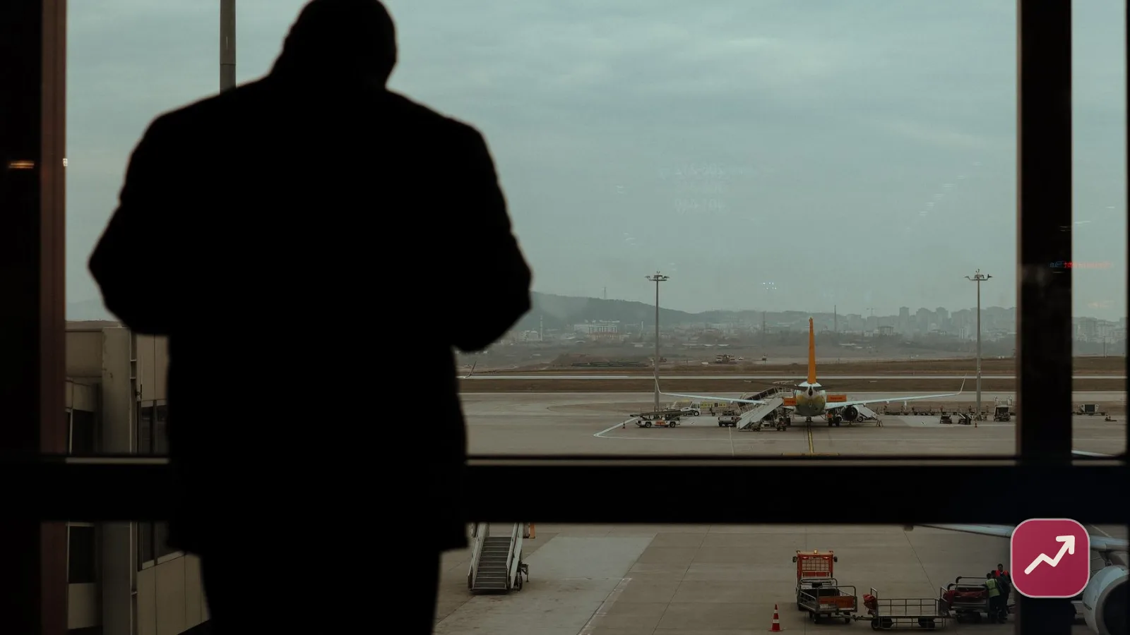 A traveller silhouetted at an airport window watching the runway, illustrating what happens to your taxes and accounts when moving abroad.