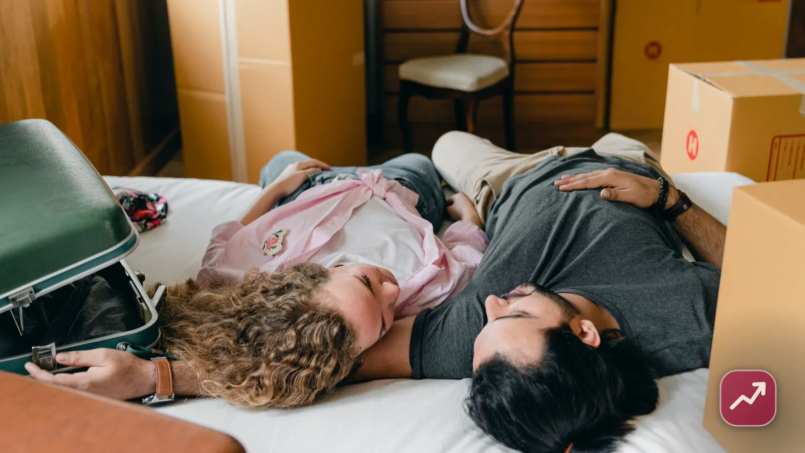 Un jeune couple non marié se repose parmi les cartons de déménagement en emménageant ensemble, illustrant ce que le PACS ou le concubinage changent pour l’argent.