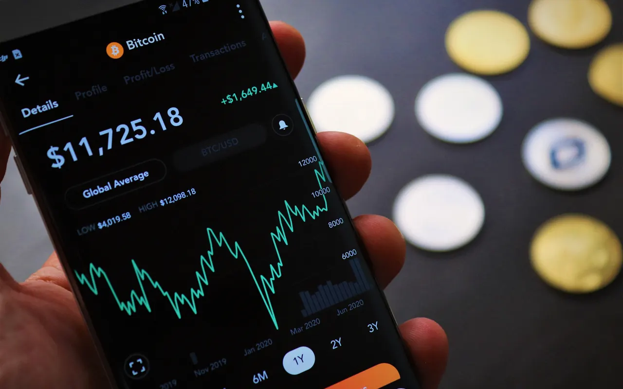 Persona revisando una app de criptomonedas en el móvil junto a un portátil
