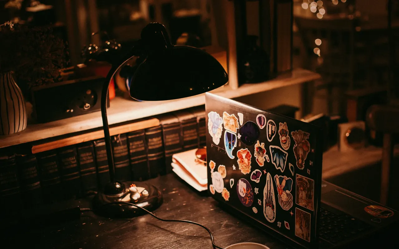 Persona tomando apuntes en un cuaderno junto a un portátil en una mesa de estudio